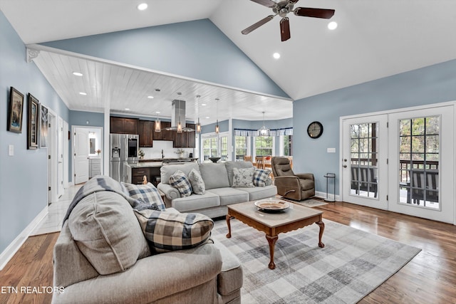 living room with ceiling fan with notable chandelier, a healthy amount of sunlight, light hardwood / wood-style floors, and high vaulted ceiling