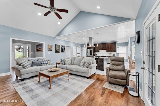 living room with light hardwood / wood-style floors, high vaulted ceiling, ceiling fan, and sink