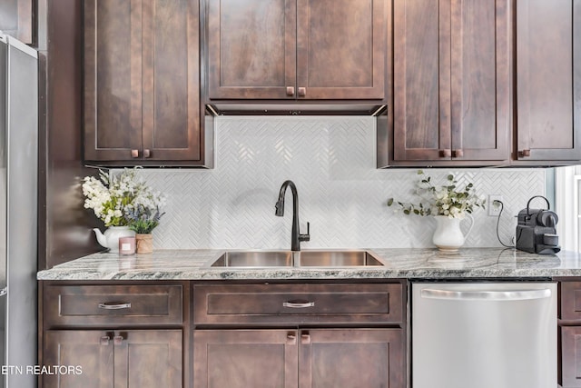 kitchen featuring sink, decorative backsplash, light stone countertops, appliances with stainless steel finishes, and dark brown cabinets