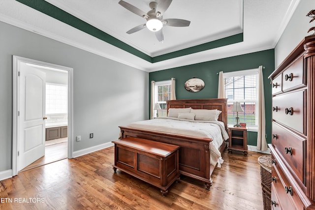 bedroom with a tray ceiling, connected bathroom, ceiling fan, and dark wood-type flooring