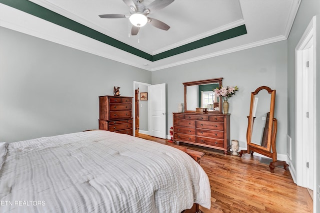 bedroom featuring hardwood / wood-style flooring, ceiling fan, crown molding, and a tray ceiling