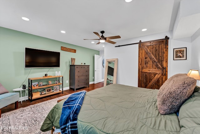 bedroom with a barn door, dark hardwood / wood-style floors, and ceiling fan