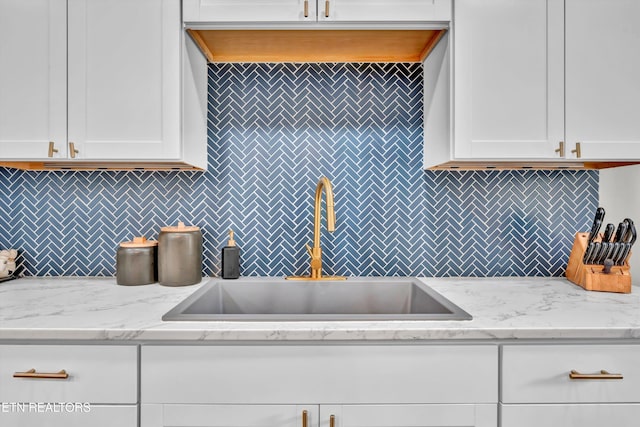 kitchen featuring white cabinets, light stone counters, and sink