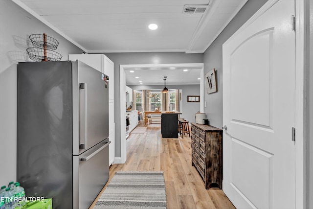 kitchen featuring stainless steel fridge, light wood-type flooring, crown molding, decorative light fixtures, and white cabinetry