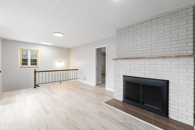 unfurnished living room featuring a brick fireplace, a textured ceiling, and light hardwood / wood-style flooring