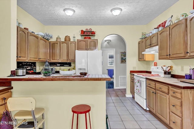 kitchen with white appliances, a kitchen breakfast bar, light tile patterned floors, a textured ceiling, and tile counters