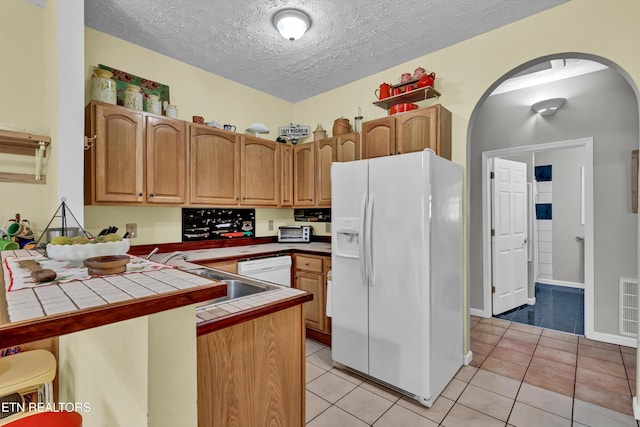 kitchen featuring kitchen peninsula, light tile patterned floors, white appliances, and tile countertops