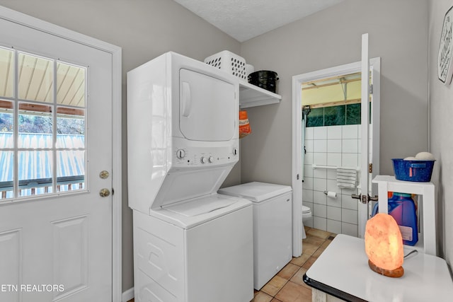 clothes washing area with stacked washer and dryer, light tile patterned floors, and a textured ceiling