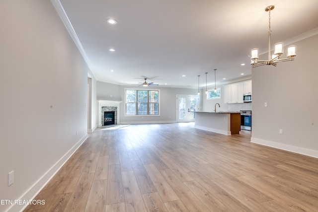 unfurnished living room featuring a stone fireplace, ceiling fan with notable chandelier, light hardwood / wood-style floors, sink, and crown molding