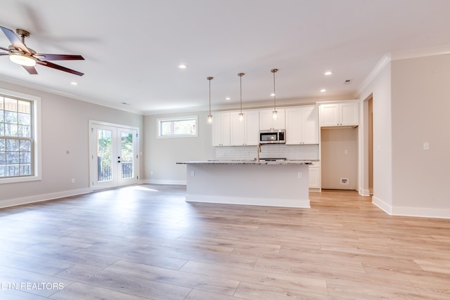 kitchen featuring pendant lighting, a healthy amount of sunlight, a kitchen island with sink, and white cabinetry