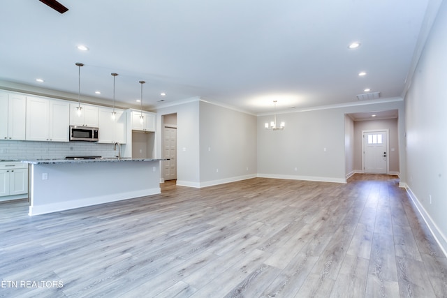 unfurnished living room with sink, light hardwood / wood-style flooring, crown molding, and a notable chandelier