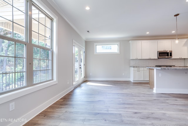 kitchen with ornamental molding, hanging light fixtures, light hardwood / wood-style flooring, white cabinets, and decorative backsplash