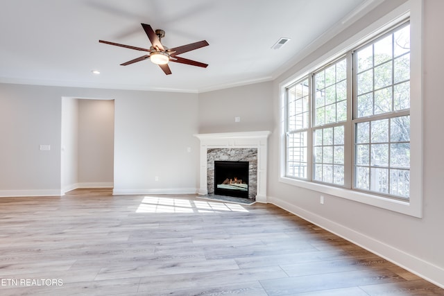 unfurnished living room featuring a high end fireplace, plenty of natural light, light hardwood / wood-style flooring, and ornamental molding