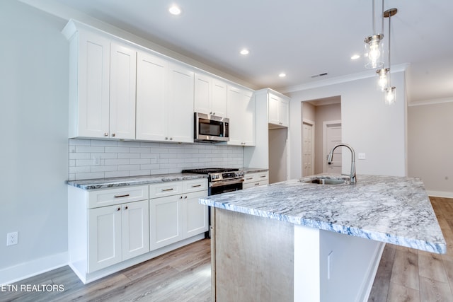 kitchen with stainless steel appliances, a center island with sink, sink, white cabinets, and pendant lighting