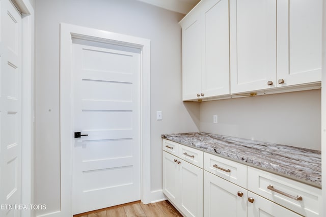 kitchen featuring white cabinetry, light stone counters, and light wood-type flooring