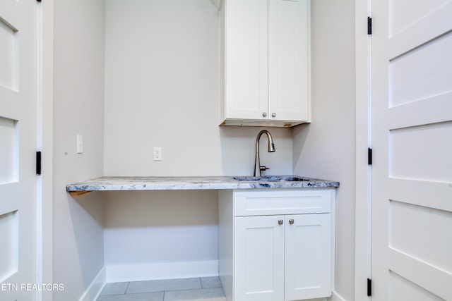 interior space featuring light tile patterned floors, white cabinetry, sink, and light stone counters