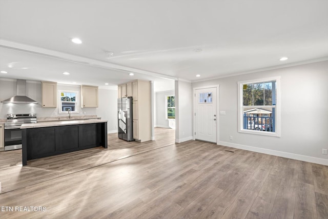 kitchen with a center island, light hardwood / wood-style flooring, ornamental molding, wall chimney range hood, and appliances with stainless steel finishes