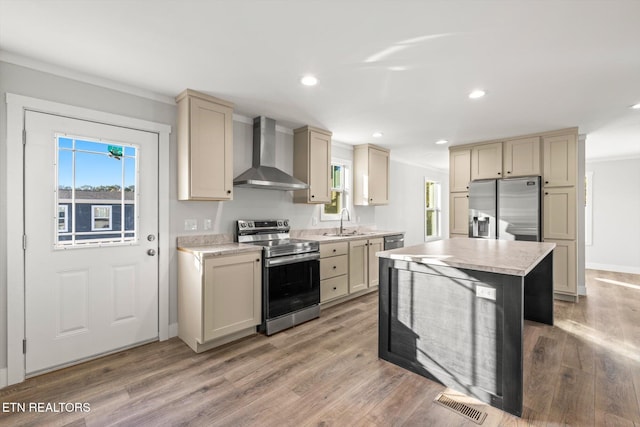 kitchen with sink, cream cabinets, appliances with stainless steel finishes, wall chimney range hood, and light wood-type flooring