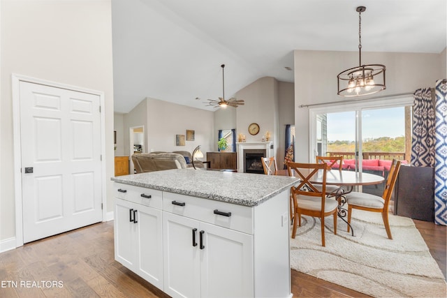 kitchen with light stone counters, pendant lighting, hardwood / wood-style flooring, white cabinets, and ceiling fan with notable chandelier