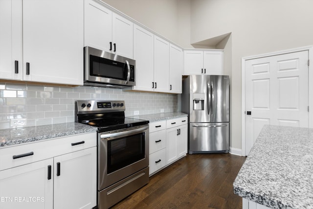 kitchen with light stone counters, dark hardwood / wood-style floors, backsplash, white cabinetry, and appliances with stainless steel finishes