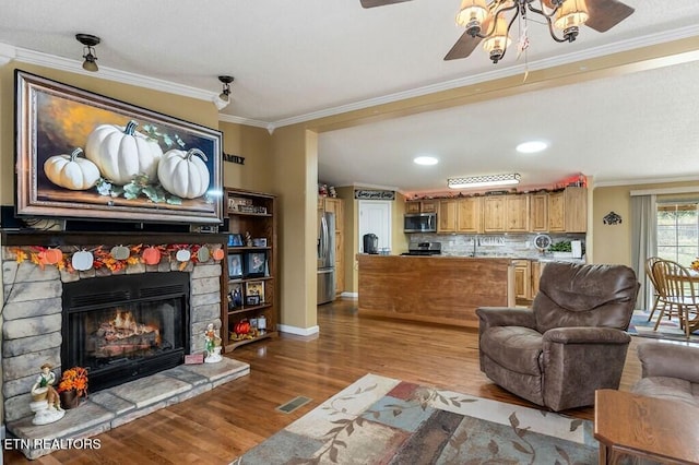 living room with a fireplace, hardwood / wood-style floors, ceiling fan, and crown molding