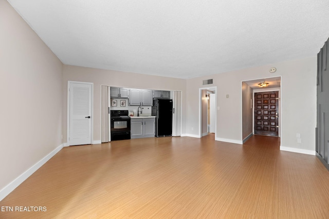 unfurnished living room with light wood-type flooring, sink, and a textured ceiling