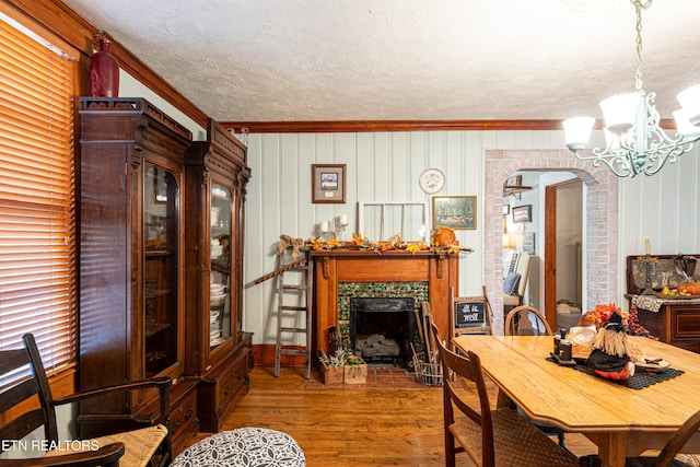 dining room with a textured ceiling, a tiled fireplace, hardwood / wood-style floors, and crown molding