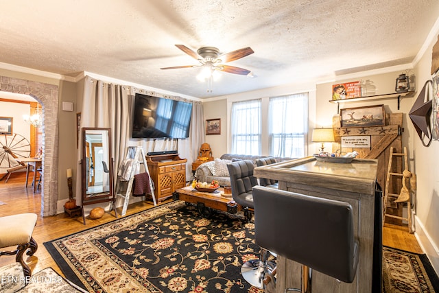 living room with ornamental molding, wood-type flooring, ceiling fan, and a textured ceiling