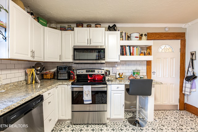 kitchen with stainless steel appliances, ornamental molding, backsplash, light stone countertops, and white cabinetry