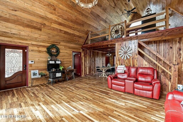 unfurnished living room featuring wood walls, hardwood / wood-style flooring, ceiling fan, and high vaulted ceiling