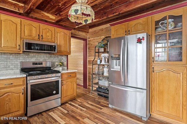 kitchen featuring wood walls, light stone countertops, appliances with stainless steel finishes, and hardwood / wood-style flooring