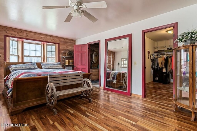 bedroom featuring wood walls, a spacious closet, wood-type flooring, and ceiling fan