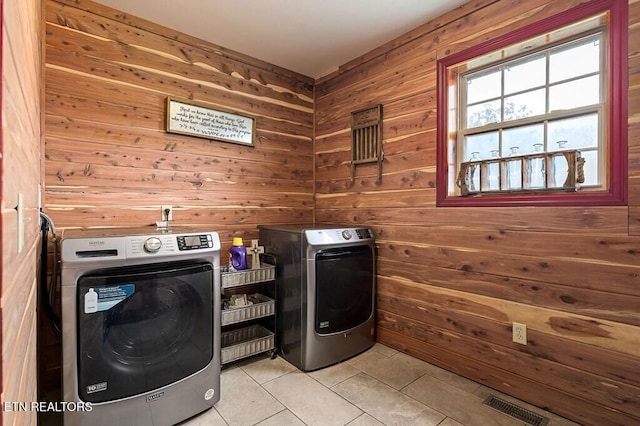 laundry area featuring washer and clothes dryer, wooden walls, and light tile patterned floors