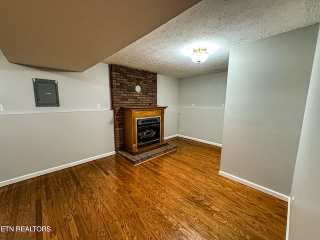 unfurnished living room featuring a brick fireplace, hardwood / wood-style flooring, electric panel, and a textured ceiling