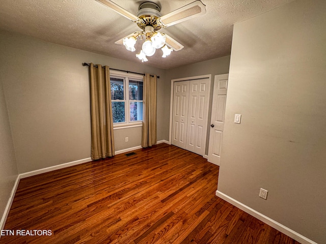 unfurnished bedroom with a textured ceiling, dark wood-type flooring, ceiling fan, and a closet