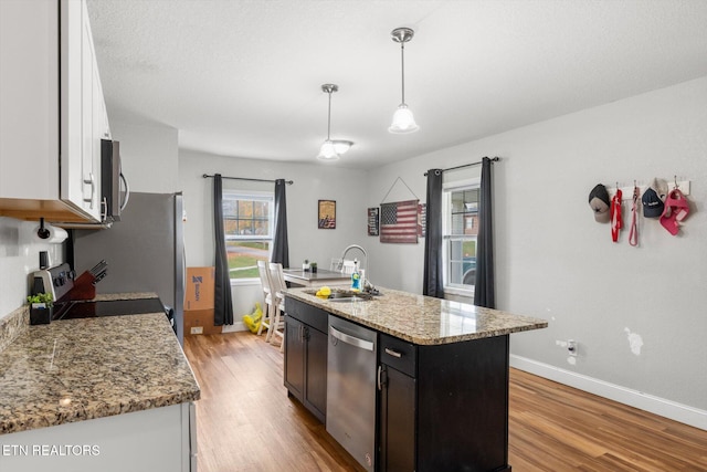 kitchen with stainless steel appliances, a kitchen island with sink, decorative light fixtures, light hardwood / wood-style flooring, and white cabinetry