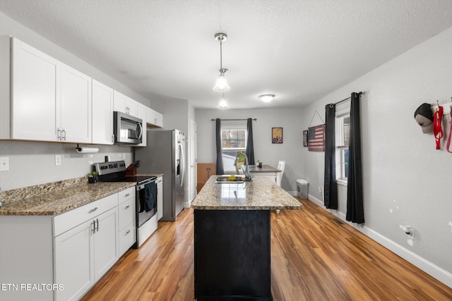 kitchen with sink, light hardwood / wood-style flooring, an island with sink, pendant lighting, and appliances with stainless steel finishes