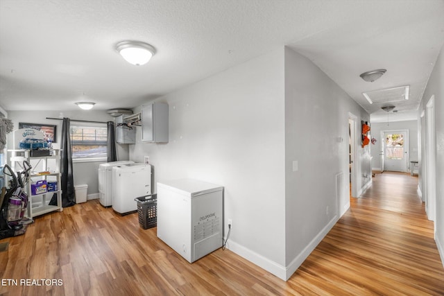 laundry area featuring washing machine and clothes dryer, a textured ceiling, and light wood-type flooring