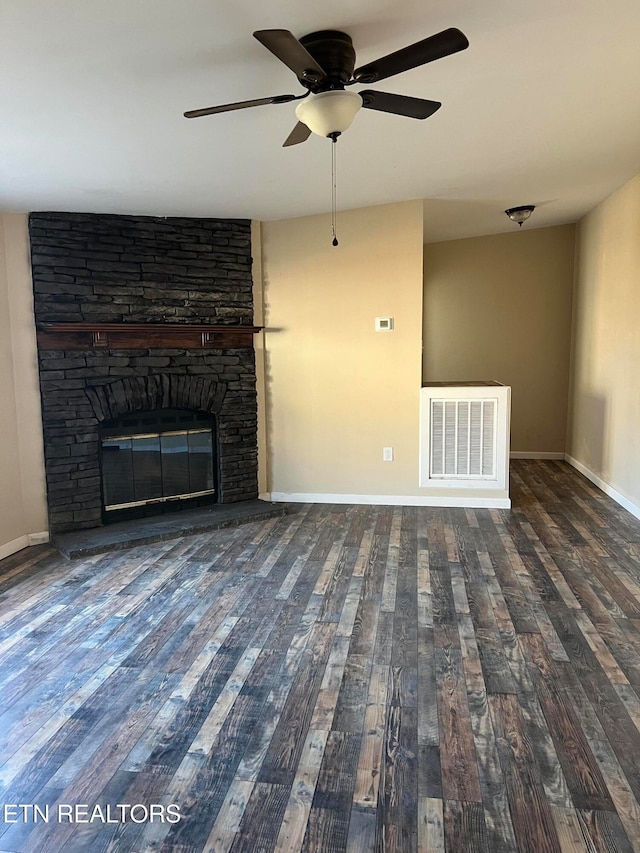 unfurnished living room with dark wood-type flooring, a stone fireplace, and ceiling fan