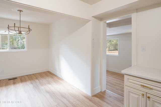 unfurnished dining area with light wood-type flooring, a chandelier, and a textured ceiling