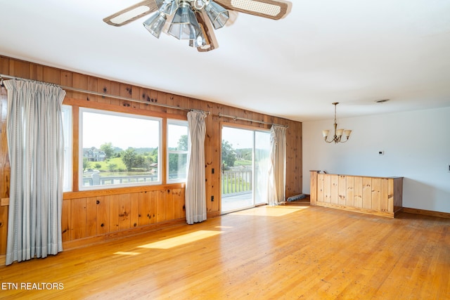 unfurnished room with ceiling fan with notable chandelier, light hardwood / wood-style floors, and wooden walls