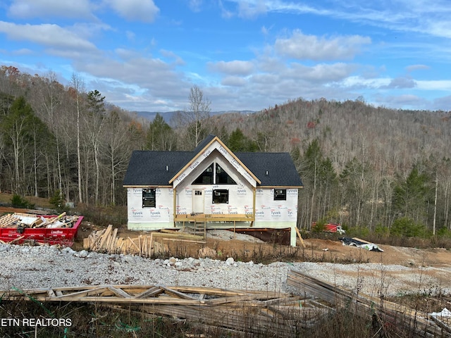 property in mid-construction featuring a shingled roof and a view of trees