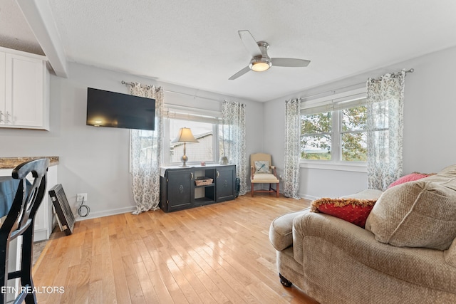 living room with a textured ceiling, light wood-type flooring, and ceiling fan