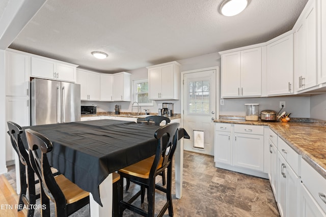 kitchen with light stone countertops, white cabinetry, a textured ceiling, and stainless steel fridge