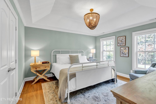 bedroom featuring a raised ceiling, a closet, light hardwood / wood-style flooring, and ornamental molding