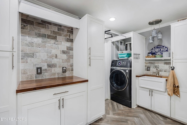 laundry area featuring cabinets, sink, ornamental molding, light parquet flooring, and washer / clothes dryer