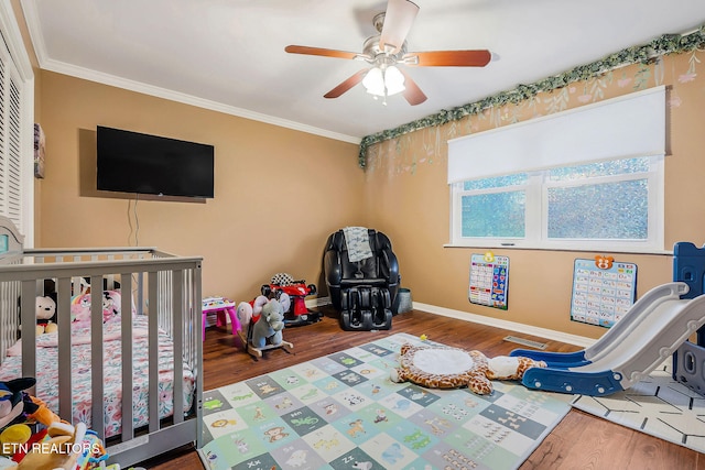 bedroom with a crib, hardwood / wood-style flooring, ceiling fan, and crown molding