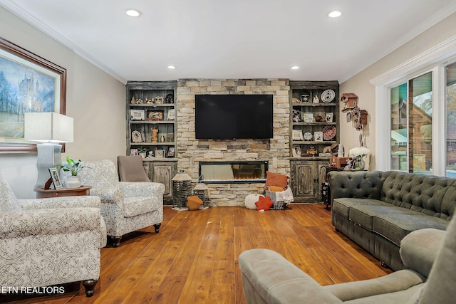 living room featuring built in shelves, a stone fireplace, hardwood / wood-style floors, and crown molding