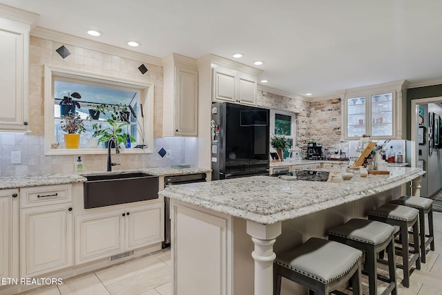 kitchen with backsplash, black refrigerator, light stone countertops, sink, and a center island