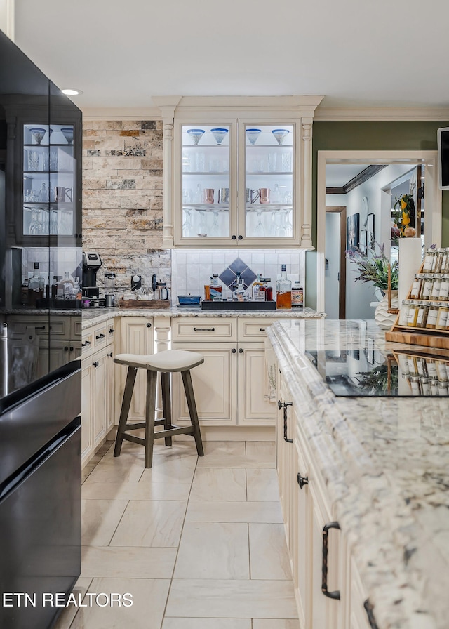 kitchen with backsplash, cream cabinets, light stone counters, and ornamental molding